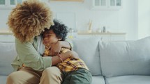 Happy African American Mother Tickling and Hugging Little Son on Sofa at Home
