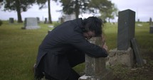 Sad, grieving man embracing family tombstone in cemetery crying in cinematic slow motion. 