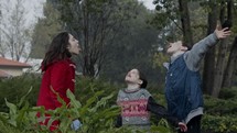 Three young kids standing enjoying the pouring rain in slow motion
