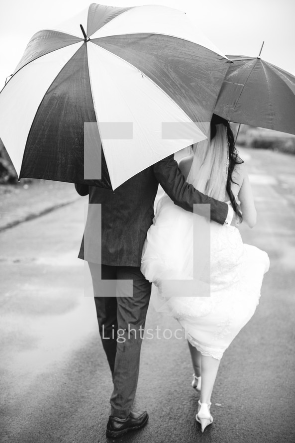 bride and groom walking with umbrellas 
