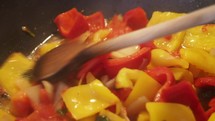 red and yellow peppers cooking in a pan, stirring with wooden spoon