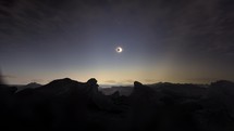 Timelapse movement of clouds above solar eclipse on rocky landscape at dusk	