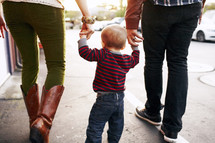 mother, father, and toddler walking holding hands