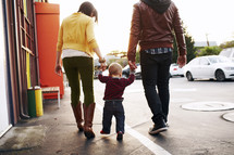 mother, father, and toddler son walking together holding hands