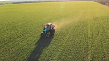 Drone footage tractor spreading artificial fertilizers in green field. Farming tractor spraying on field with herbicides. Industrial machine fertilizing a field. Chemicals used by agricultural tractor.