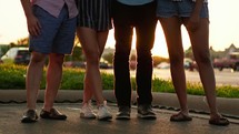legs of a group of friends standing together with arms around each other 