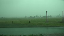 Heavy, dramatic, slow motion rain falling on green, summer or spring grass on rural America farmland. Rain waters crops and grass after drought in farming community.