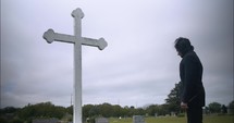 Young man in black suit looking at cross praying in worship in cinematic slow motion.