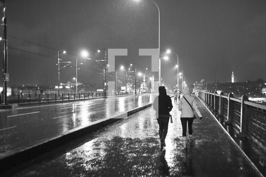 Two people walking over a bridge during a stormy night