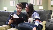 a young couple reading a Bible together on a couch 