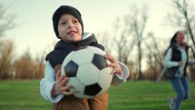 Cheerful boy with black and white soccer ball In his hands run in the park. Slow Motion. Kid plays in the park.