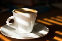 a cup of coffee in sunlight on a table 