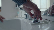 Man turning faucet handle, washing hands and rinsing face with water above the sink in bathroom at home. Close-up shot
