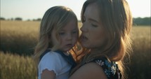 Young mother holding her daughter in summer sunset.