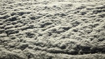 View of earth and clouds from airplane window while flying in cinematic slow motion above the clouds in the atmosphere.