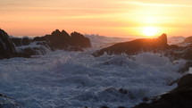 waves crashing into a shore at sunset 