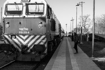 Black and white photograph of a train arriving while people wait.