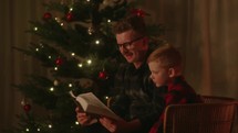 Father and son reading the bible together by the Christmas tree