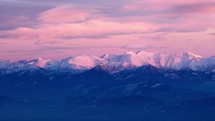 Snowy peaks of mountain peaks in pastel colors at dusk. Telephoto shot, timelapse