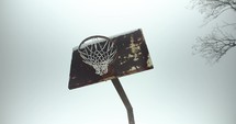 Old, rusty basketball hoop and court on snowy day. Slow motion snow and snowflakes fall in winter storm in small town.