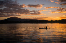 A boat is rowed in a river lit by the sunset.