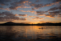 A person rowing along a river while the sun sets.