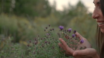 Young Woman Smells Purple Flowers in Meadow at Sunset - Close Up