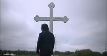 Young man in black suit looking at cross praying in worship in cinematic slow motion.