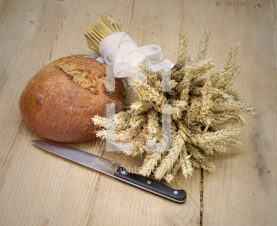 Loaf of Bread with Bundle of Cereals on Wooden Background