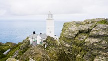 Beautiful White Lighthouse On A Rocky Cliff Looking Over Calm Blue Ocean Water