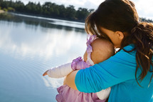 mom hugging baby daughter by a lake