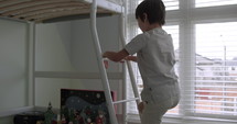 Young boy climbs up ladder into his bunk bed