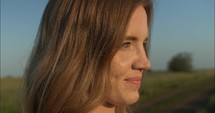 Happy, smiling woman watching sunset on farm in summer sunset.