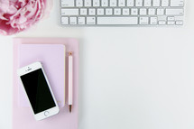 computer keyboard, iPhone, pen, journal, and pink peony on a white background 