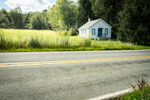 Paved rural road in front of quaint old community building with grassy yard 