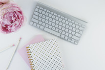 computer keyboard, iPhone, pen, journal, and pink peony on a white background 