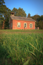 Old brick one room schoolhouse with grassy yard and wooden fence 