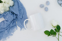 white roses, blue scarf, speckled blue eggs, white background, coffee mug