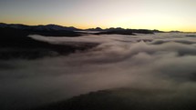 Aerial shot drone flies over fog covered valley just before sunrise