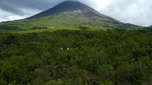 Aerial shot drone flies up and away from volcano in lush green rainforest