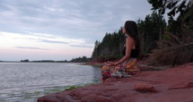 Young woman sitting on rocks at edge of ocean meditating - side profile