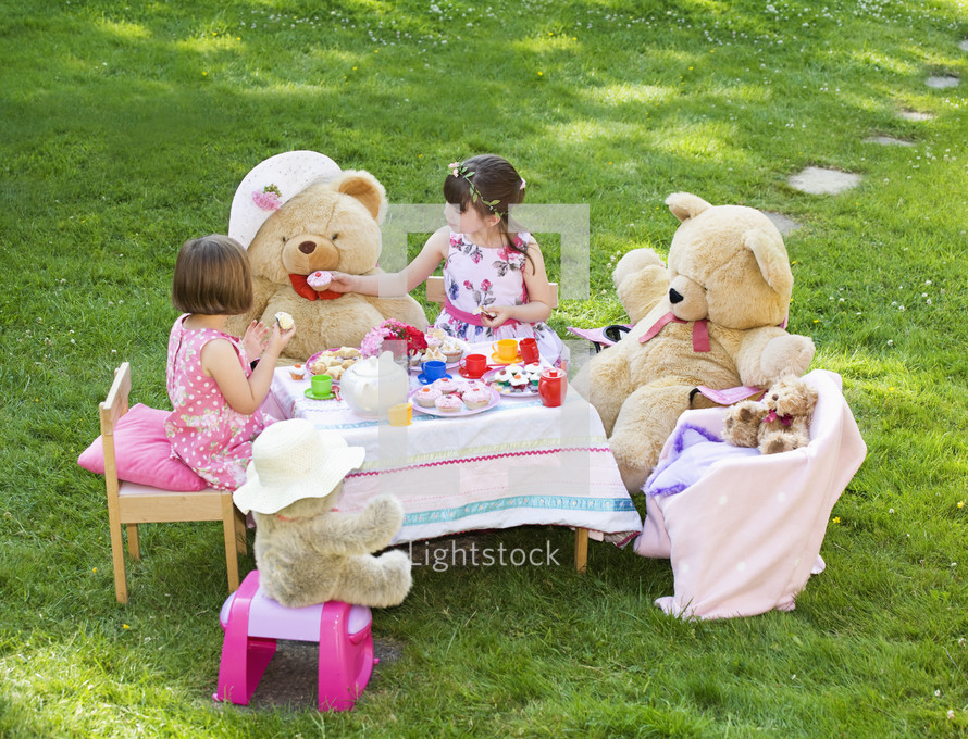 Elevated view of two young girls playing Teddy Bears Picnic in their back garden themes of imagination daydreaming playing
