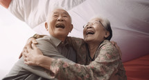 AI Generated Image. Happy Asian Senior elderly couple hugging against the parachute