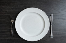Empty plate with a fork and knife on a dark wood table