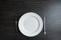Empty plate with a fork and knife on a dark wood table