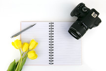 yellow tulips, notebook, blank pages, pen, and camera 