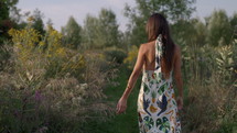 Woman taking walk through nature path with flowers during summer sunset