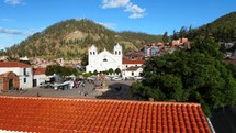 Aerial shot drone ascends up over plaza with white church and terracotta roof