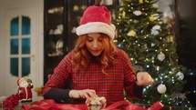 Girl is wrapping Christmas presents in front of the tree