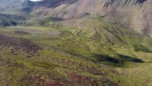 Aerial shot drone flies forward over green hills toward large brown mountain